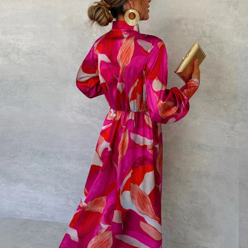 Outfit completo con vestito lungo fucsia stampa astratta, accessori dorati e décolleté nude, look elegante da sera
