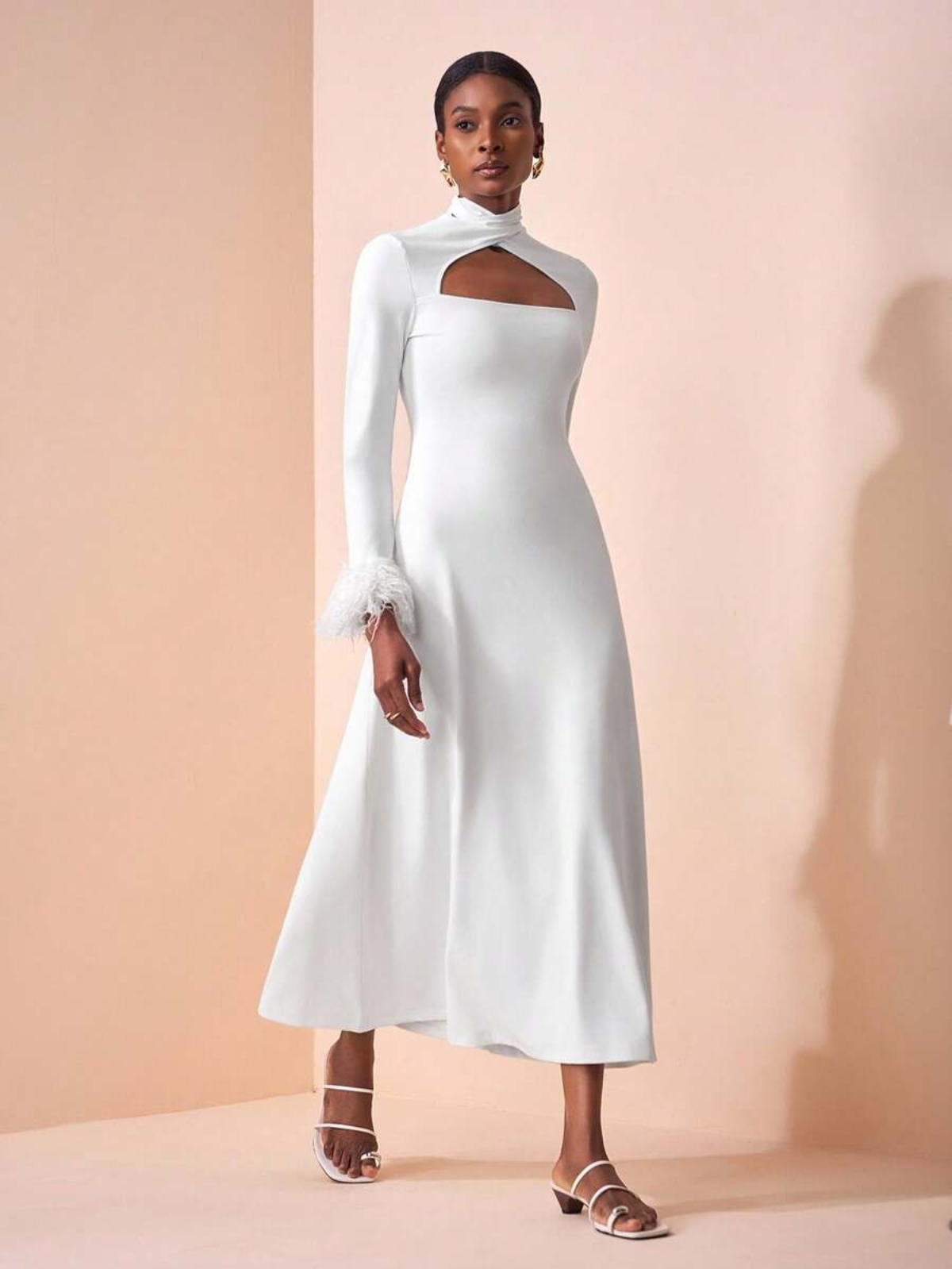 Dettaglio abito con collo alto e cut-out geometrico, tessuto stretch, finiture in piume sui polsi, styling minimalista ed elegante.
