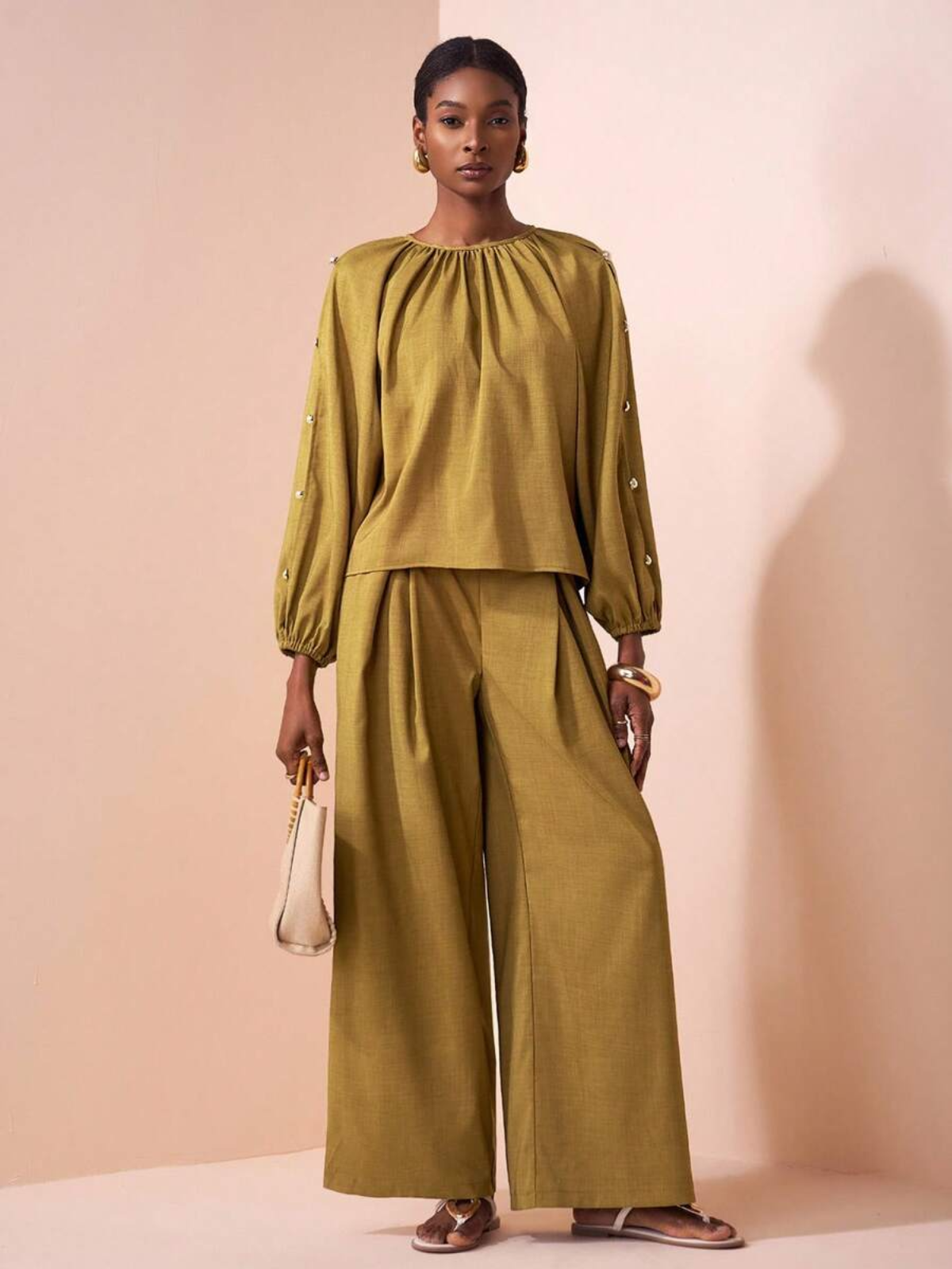 Dettaglio completo senape con bottoni perla decorativi sulle maniche, tessuto fluido, styling minimalista con borsa a mano beige
