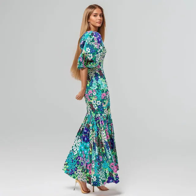 Vestito lungo floreale multicolor con maniche a sbuffo, stampa vivace blu verde viola, su sfondo neutro
